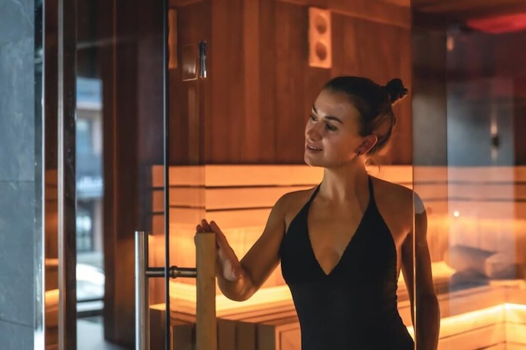 mujer saliendo de sauna con puertas de vidrio y luces LED